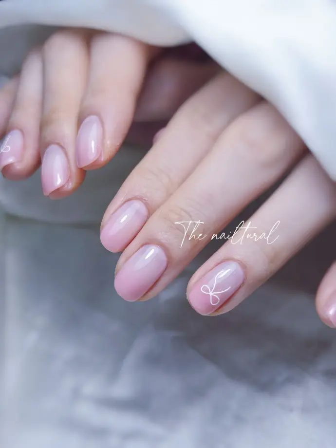 oval nails, a sheer pink manicure , delicate, hand-painted white artwork, minimalist, flowing white line , a ribbon, artistic touch soft pink, drawing attention , hand-drawn detail