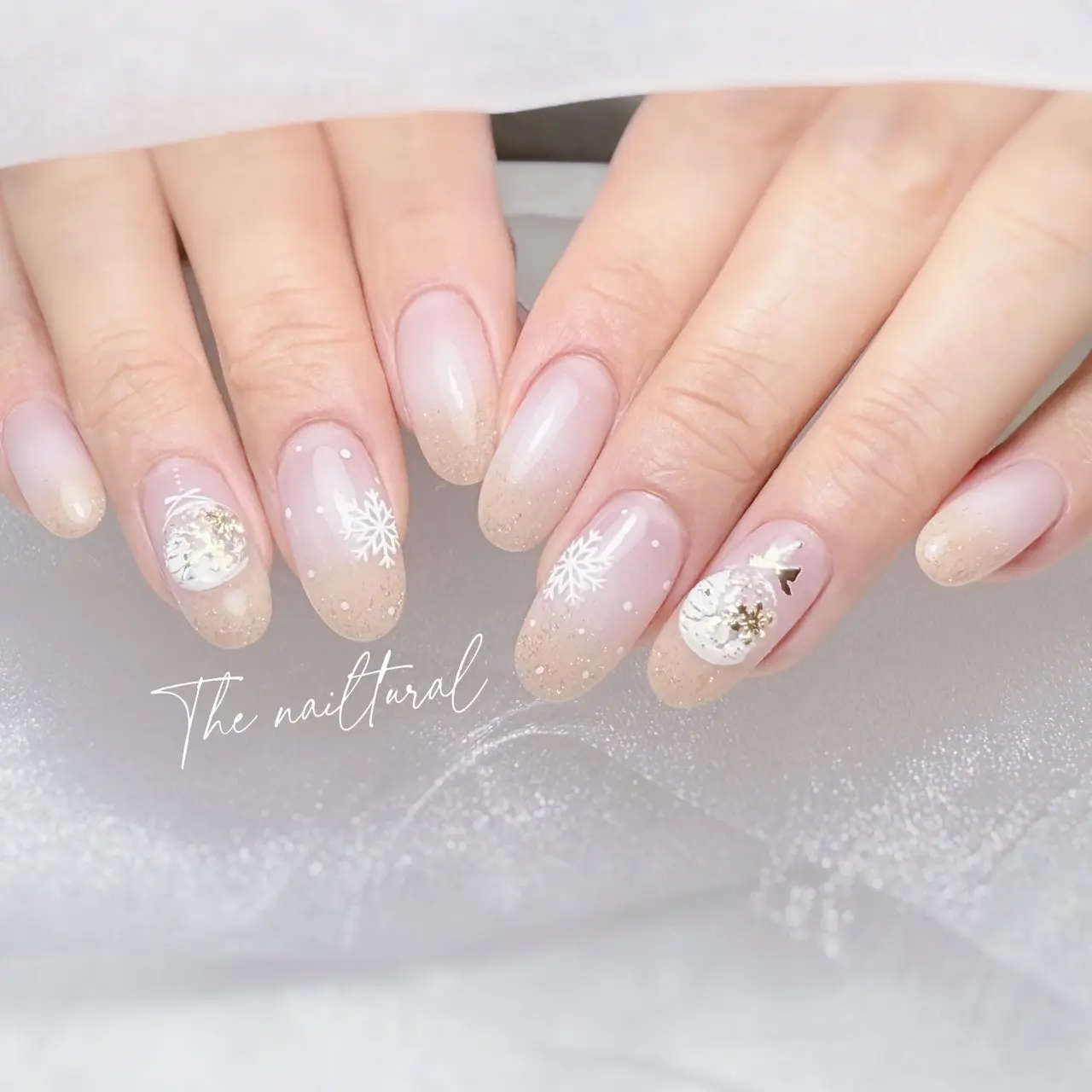 oval-shaped nails , delicate winter nail art ,  festive-themed nail art soft gradient, transitioning pale nude , shimmer towards the tips. snowflakes, stylised winter scenes , gold accents, snow-covered nail art,  resembling falling snow, elegant and seasonal nail art, 