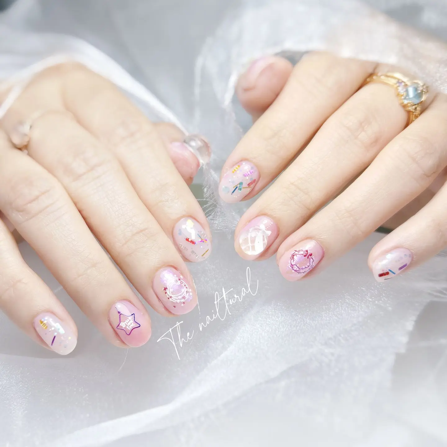 short oval-shaped nails , playful and colorful nail art  sheer, light pink base,  whimsical decals,  stars with faces, moons, planets, highlighting the fun and imaginative nail designs